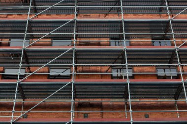 Ön cephe tamiri için iskeleli kırmızı tuğla duvar. Şehir ortamında bina bakımı, restorasyon ve yenilemeyi ön plana çıkaran kentsel inşaat sahası.