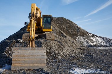 Heavy-duty excavator shovel on a gravel mound at a construction site, front view of industrial work, earthmoving shovel and development under a clear blue sky. clipart