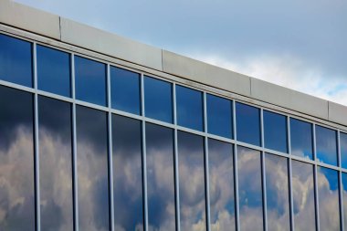 Contemporary office building with large reflective glass windows mirroring cloudy skies, showcasing modern architecture and urban design. clipart