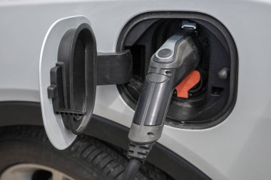Kabloyu şarj ederek şarj eden beyaz bir elektrikli arabanın kapanışı. EV, ulaşım ve sürdürülebilir teknoloji temaları için modern temiz enerji kavramı.