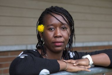 Saçları örgülü Afrikalı bir kadın portresi kulağının arkasına saklanmış sarı bir karahindiba çiçeği ve sakin bir ifade. Güzellik, doğal ve açık hava yaşam tarzı temaları için mükemmel..