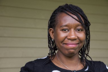 Saçı örgülü, mutlu ve açık havada kendinden emin görünen mutlu, gülümseyen Afrikalı bir kadının portresi. Mutluluk için ideal, otantik yaşam tarzı, çeşitlilik ve pozitiflik temaları.