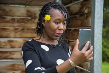 Saçları örgülü ve sarı çiçekli sürpriz Afrikalı kadın. Dışarıdan bir video görüşmesi yapıyor. Sanal toplantılar, teknoloji kullanımı, çevrimiçi iletişim ve modern yaşam tarzı kavramları için mükemmel..