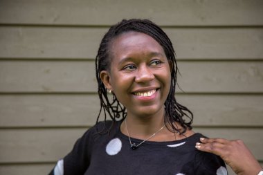 Saçları örgülü mutlu Afrikalı kadın gülümsüyor ve yan tarafa bakıyor, omuz omuza, tahta duvara karşı duruyor. Yaşam tarzı, pozitiflik, çeşitlilik, moda ve reklam kullanımı için mükemmel.