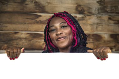 Güler yüzlü siyah kadın boş tahtayı kırsal ahşap arka planda sunuyor, promosyon içeriği için mükemmel.