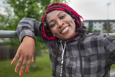 Renkli, koruyucu saç stili olan neşeli siyahi bir kadın. Korkuluklara yaslanıyor. Yaşam tarzı ve konsepti için mükemmel.