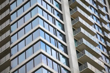 Mavi gökyüzüne karşı geometrik pencere desenli modern cam ofis cephesi. Çağdaş şehir mimarisi gösterişli kule tasarım detaylarını gösteriyor.