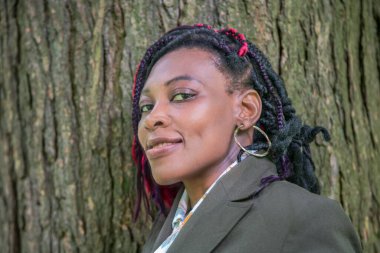 Özgün bir Afrikalı kadın portresi. Ağaç kabuğuna karşı kırmızı örgülü. Kültürel miras, kimlik ve hakiki güzelliğin ön plana çıkarıldığı doğal ortam..