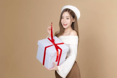 Genç Asyalı, uzun saçlı, bereli, güzel yüzlü, temiz tenli, izole edilmiş bej bir kadın. Kadın model elinde hediye kutuları, yüz bakımı, kozmetoloji, estetik cerrahi..