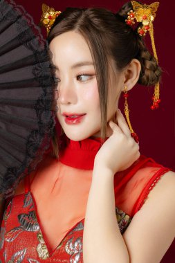 Temiz tenli güzel bir Asyalı kadın geleneksel Cheongsam Qipao elbisesi giyiyor ve elinde kırmızı arka planda poz veriyor. Stüdyoda kadın modelin portresi. Mutlu Çin Yeni Yılı.