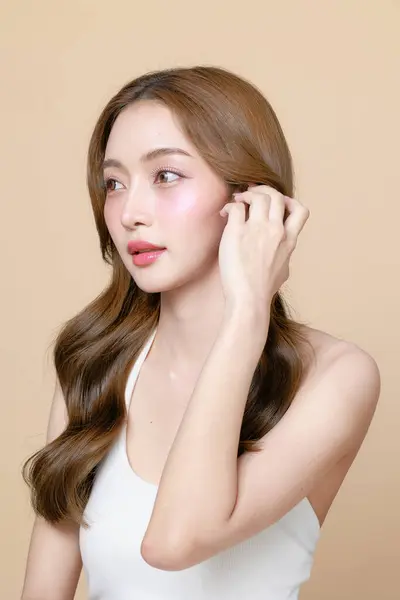 韓国のメイクスタイルの若いアジアの美女カーリーロングヘアは 孤立したベージュの背景に彼女の顔と完璧な肌に触れます フェイシャルトリートメント プラスチック手術 — ストック写真