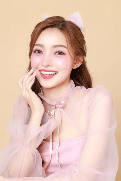 stock image Young cute Asian woman in a pink elegant dress, Korean style makeup, moisturized, smooth, perfect skin on a beige background. Facial treatment, Cosmetology, plastic surgery.