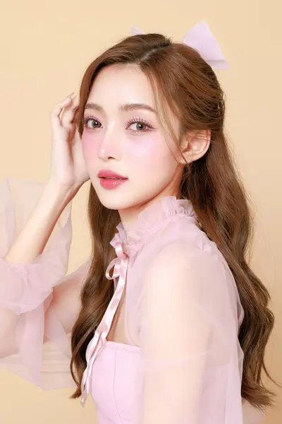 Stock image Young cute Asian woman in a pink elegant dress, Korean style makeup, moisturized, smooth, perfect skin on a beige background. Facial treatment, Cosmetology, plastic surgery.