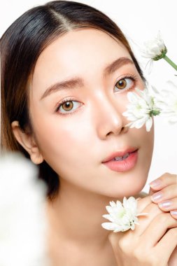 Güzel bir yüzü, pürüzsüz bir teni ve çiçeği olan Asyalı kadını yakından çek. Doğal makyajı ve ışıl ışıl gözleri olan sevimli bir kadın model beyaz izole edilmiş arka plandaki kameraya bakıyor..