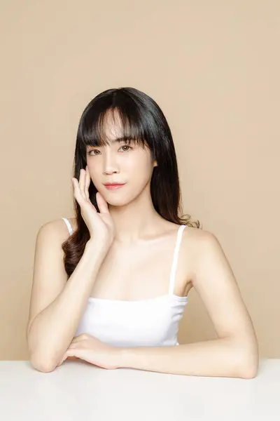 韓国のメイクスタイルの若いアジアの美女カーリーロングヘアは 孤立したベージュの背景にブラシを使用して彼女の顔と完璧な肌に触れます フェイシャルトリートメント プラスチック手術 — ストック写真