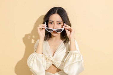 Güzel yüzlü ve mükemmel temiz tenli Asyalı bir kadın. Bej izole arka planda, seksi elbiseli, lüks modaya uygun bir kadın model. Kozmetoloji, E-ticaret, Çevrimiçi alışveriş kavramı.