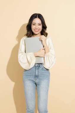 Mükemmel vücutlu Asyalı mutlu kadın stüdyoda dizüstü bilgisayarı kullanıyor. Bej izole arka planda, seksi elbiseli, lüks modaya uygun bir kadın model. E-ticaret, Online alışveriş kavramı.