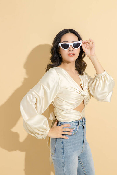 Asian woman with a beautiful face and Perfect clean fresh skin. Luxury fashionable female model in sexy dress with on beige isolated background. Cosmetology, E-commerce, Online shopping Concept.