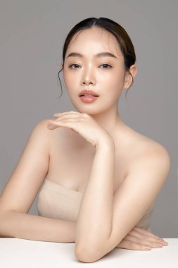 Güzel, genç, Asyalı bir manken, gri arka planda tertemiz bir ciltle yüzüne dokunuyor. Yüz bakımı, yüz bakımı, kozmetik, estetik cerrahi stüdyoda güzel bir kız portresi..