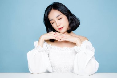 Mükemmel temiz cilde sahip Asyalı kısa saçlı bir kadın. Doğal makyajı ve mavi izole edilmiş arka planda ışıl ışıl gözleri olan sevimli bir kadın modeli. Yüz bakımı, kozmetoloji, güzellik konsepti..