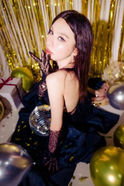 Seksi siyah elbise giyen genç çekici Asyalı kadın, balonlu, parlak altın parıltılı arka planda lüks hediye kutularıyla yapılan partiyi kutluyor. doğum günü, yeni yıl konsepti.