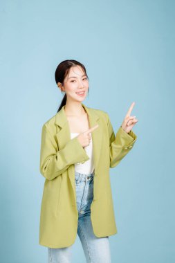 Mutlu gülümseyen, başarılı, 20 'li yaşlarda, sıradan, yeşil moda ceketli iş kadını pastel mavisi arka planda izole edilmiş bir yeri işaret ediyor. Kadın girişimciler, ofis çalışanı konsepti.