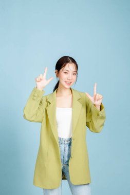 Mutlu gülümseyen, başarılı, 20 'li yaşlarda, sıradan, yeşil moda ceketli iş kadını pastel mavisi arka planda izole edilmiş bir yeri işaret ediyor. Kadın girişimciler, ofis çalışanı konsepti.