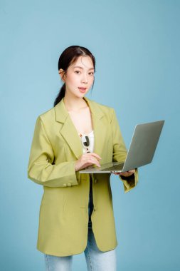 Mutlu, mutlu, mutlu, 20 'li yaşlarda, sıradan yeşil moda ceketli ve dizüstü bilgisayarı mavi arka planda olan başarılı bir çalışan kadın. Kadın girişimciler ya da ofis çalışanı konsepti.