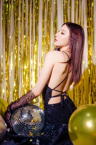 年轻迷人的美丽的亚洲女人穿着时尚性感的黑色礼服 喜欢在派对上摆设豪华礼品盒 背景上闪烁着金光闪闪的气球 新年概念 — 图库照片