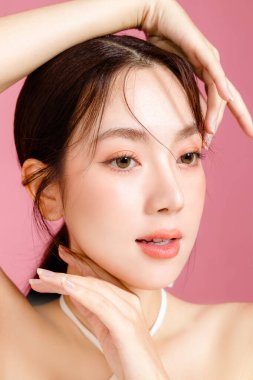 Yüzünde doğal makyajla bir araya gelen genç Asyalı kadın dolgun dudaklara ve soyutlanmış pembe arka planda beyaz gecelik giyen taze bir tene sahip. Stüdyoda güzel bir kadın modelin portresi..