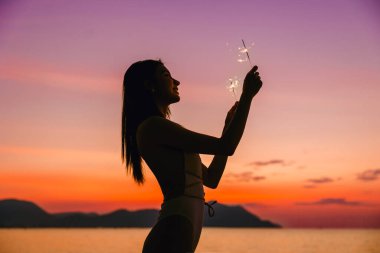 Mayo giymiş, havai fişeklerle rahatlayıp plaj tatilinin tadını çıkaran mutlu, zayıf kadının yan görüntüsü. Yaz seyahati.