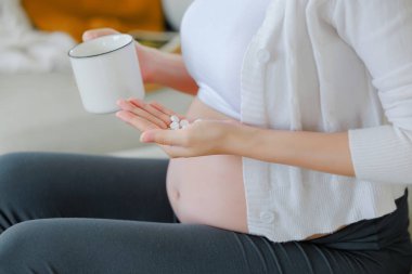 Kanepeye ilaç koyup karnına dokunan Asyalı mutlu hamile kadının elini kapat. Aile planı, hamilelik, annelik, insanlar ve beklentiler, çocuk ve doğum öncesi bakım konsepti.