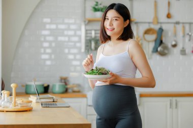 Hamilelik, sağlıklı yiyecekler ve insan konsepti. Mutlu hamile bir kadının evde kahvaltıda sebze salatası yemesi. Çocuk ve Doğum Öncesi Bakım kavramı.