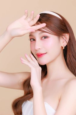 Güzel Asyalı, kıvırcık saçlı, uzun kıvırcık saçlı, Koreli makyajlı, yüzü parlayan ve bej arkaplanda sağlıklı bir yüz portresi olan bir kadın. Kozmetik, estetik cerrahi.