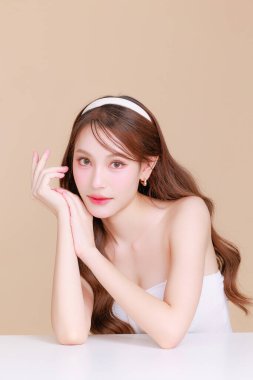 Güzel Asyalı, kıvırcık saçlı, uzun kıvırcık saçlı, Koreli makyajlı, yüzü parlayan ve bej arkaplanda sağlıklı bir yüz portresi olan bir kadın. Kozmetik, estetik cerrahi.