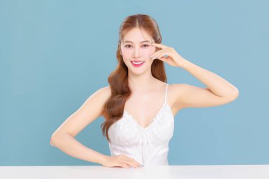 Pretty Asian beauty woman curly long hair with Korean makeup glowing face and healthy facial skin portrait smile on isolated blue background. clipart