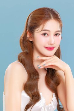 Pretty Asian beauty woman curly long hair with Korean makeup glowing face and healthy facial skin portrait smile on isolated blue background. clipart