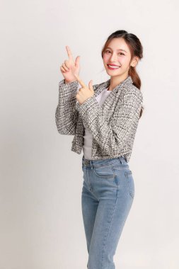 Gülümseyen Asyalı genç iş kadını lider girişimci şık bir takım elbise giyip izole edilmiş arka planda ürün veya metin için parmakla işaret ediyor.