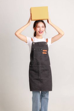 Gülümseyen Asyalı genç iş sahibi kadın lider girişimci şık bir önlük giyerek izole bir arka planda sipariş vermek için paket kutusu tutuyor..