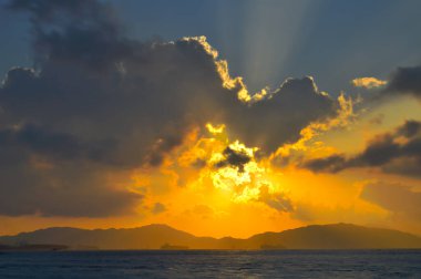 Güneş ışınları denizin üzerinde bulutların arasından fışkırıyor.