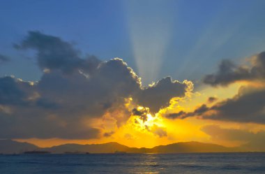 Güneş ışınları denizin üzerinde bulutların arasından fışkırıyor.
