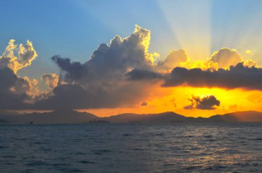 Güneş ışınları denizin üzerinde bulutların arasından fışkırıyor.