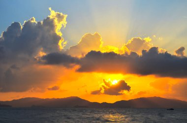 Güneş ışınları denizin üzerinde bulutların arasından fışkırıyor.