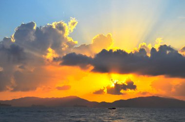 Güneş ışınları denizin üzerinde bulutların arasından fışkırıyor.