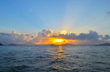 Güneş ışınları denizin üzerinde bulutların arasından fışkırıyor.