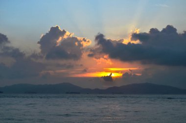 Güneş ışınları denizin üzerinde bulutların arasından fışkırıyor.