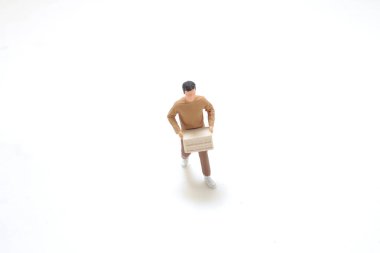 Minyatür figür, düz bir alana kurulmuş bir karton kutu tutarken resmedilir.