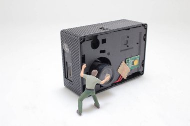 Büyük bir elektronik kamera bileşenini tamir etmeye çalışan minyatür figür resmedildi,