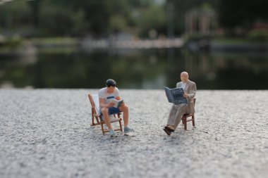 Minyatür figürler dışarıda, sakin bir gölün yanında oturuyorlar.,