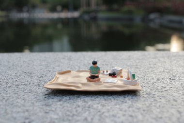 tiny figurine depicted enjoying a serene picnic by the lake. clipart